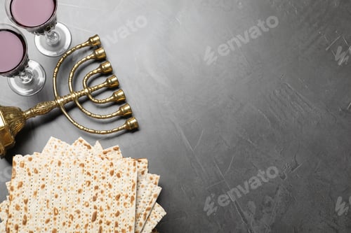 Preview: Stack of traditional matzos, red wine and menorah on grey table, flat lay. Space for text