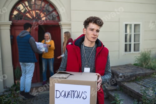 Preview: Group of young volunteers giving donation box to senior woman standing in door, social care concept