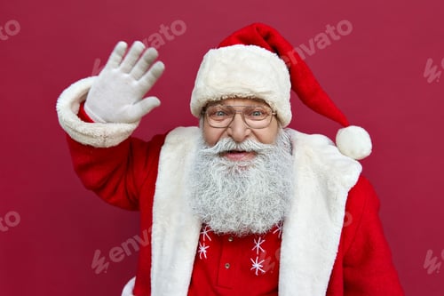 Preview: Happy Santa Claus wearing costume waving hand looking at camera.