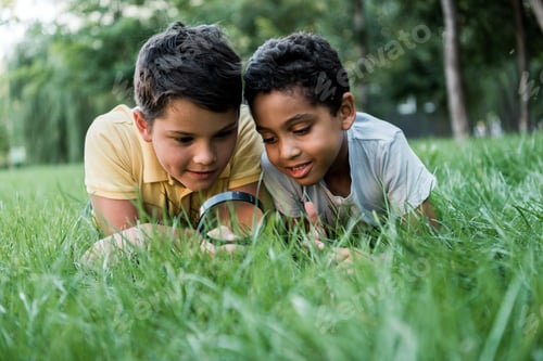 Preview: selective focus of multicultural boys lying on grass and looking through magnifier
