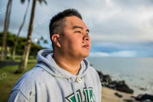 Preview: Young man looking out at sunrise from Kaaawa beach, Oahu, Hawaii, USA