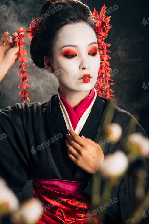 Preview: selective focus of geisha in black kimono with red flowers in hair and sakura branches on black