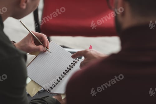 Preview: cropped image of man pointing on something in friends notebook in library
