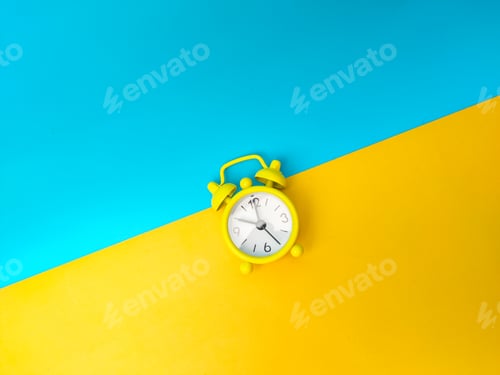 Preview: Top view yellow alarm clock on a yellow and blue background.