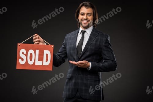 Preview: professional young businessman showing sold sign and smiling at camera isolated on black