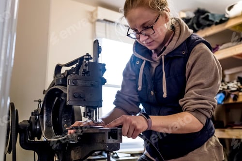 Preview: Female saddler standing in workshop, sewing leather strap on saddlery sewing machine.