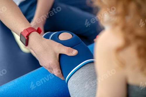 Preview: Male physiotherapist hands holding knee bandage of female patient sitting on couch with knee bolster