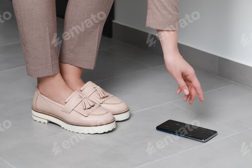 Preview: Woman taking dropped smartphone from floor, closeup. Device repairing