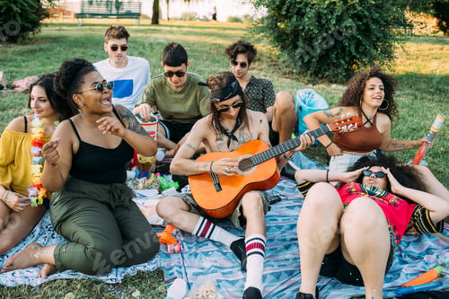 Preview: Group of friends relaxing, playing guitar at picnic in park