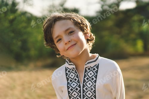 Preview: A boy smiles confidently while standing in a sunlit field, wearing a traditional embroidered shirt