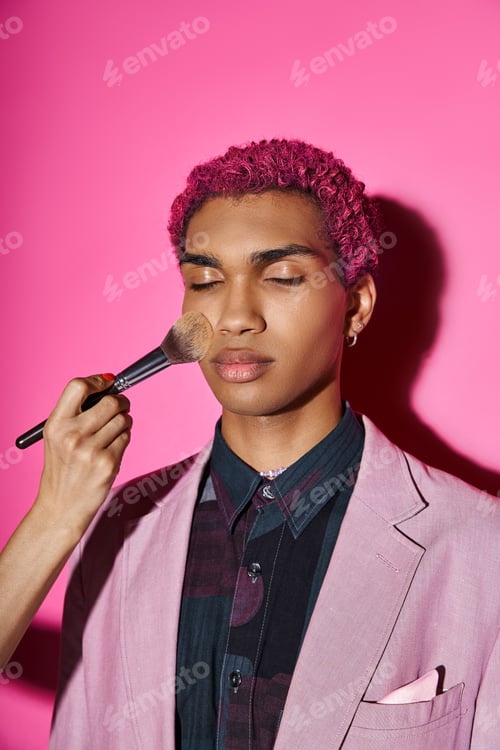 Preview: handsome man with curly pink hair posing with closed eyes, hand with makeup brush, doll like