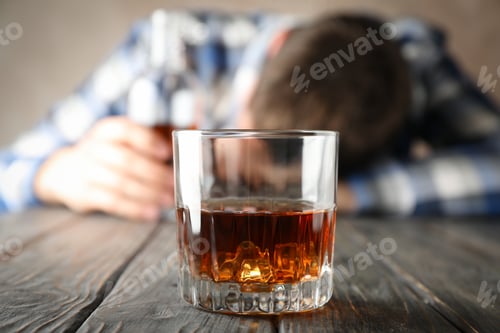 Preview: Glass of whiskey against drunk man on wooden background, close up