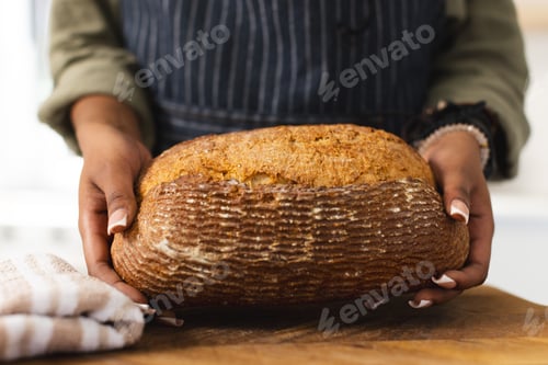 Preview: African American young woman holding freshly baked bread at home with copy space