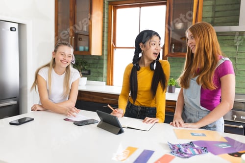 Preview: Teen girls laughing and studying together at home with tablet and notebooks