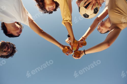 Preview: Upside down. View from below of people that are cheering with beer bottles