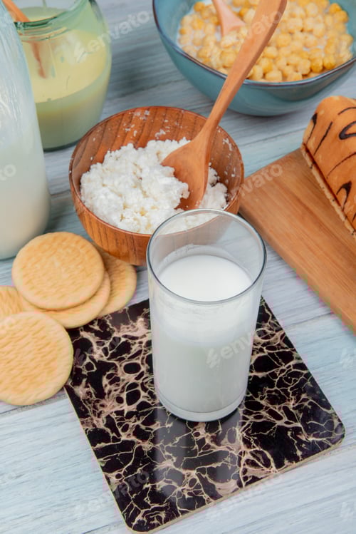 Preview: side view of glass of milk with cookies, condensed milk, cottage cheese, roll, cereals on wooden