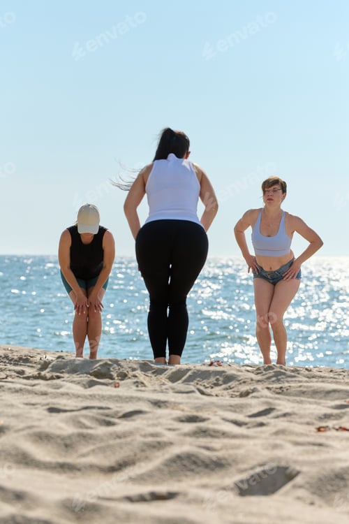 Preview: Group yoga stretching on Sandy Beach by Baltic Sea under clear sky