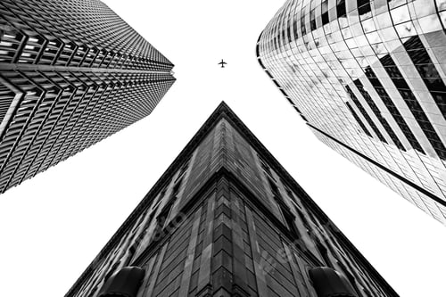 Preview: Three tall buildings shot from a low angle with an airplane in black and white