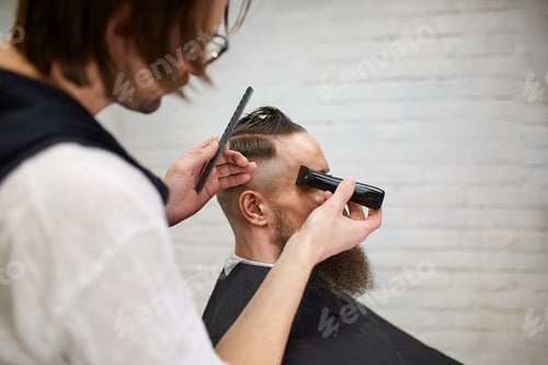 Preview: Master cuts hair and beard of men in the barbershop, hairdresser makes hairstyle for a young man