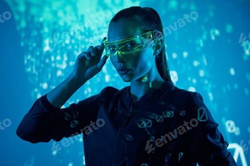 Preview: Confident young woman adjusting futuristic glasses against colorful background