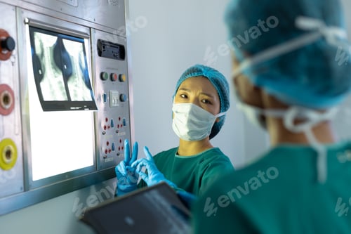 Preview: Two diverse female surgeons discussing x-ray on lightbox in operating theatre