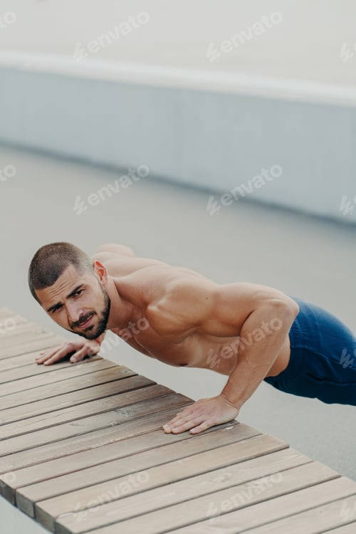Preview: muscular bearded man stands in plank pose trains chest and arms muscles has hard workou