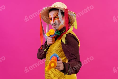 Preview: Clown with white facial makeup on a pink background, playing with toy guns and hat