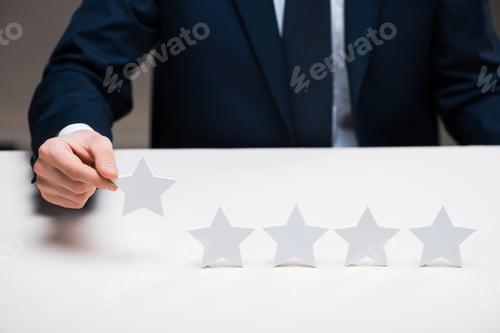 Preview: cropped view of businessman in suit holding star on grey, quality concept