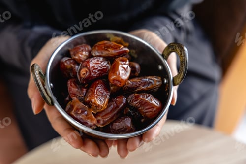Preview: Young woman's hand offering dried dates in a cup