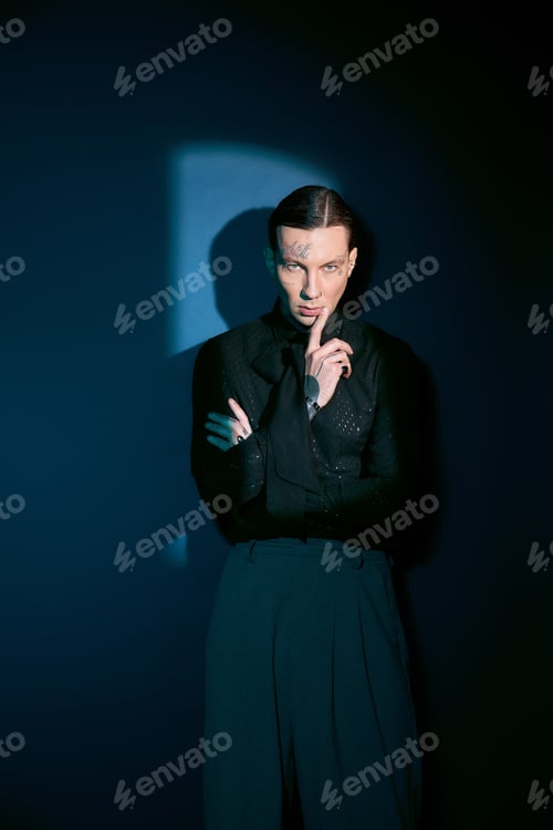 Preview: Stylish young man posing confidently in striking attire against a dark blue backdrop