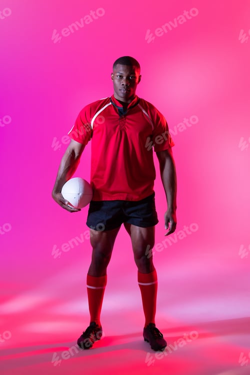 Preview: Portrait of african american male rugby player with rugby ball over pink lighting