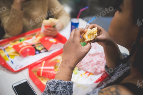 Preview: young african woman eating sandwich with friends in fast food