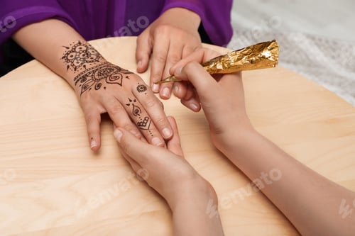 Preview: Master making henna tattoo on hand at wooden table, closeup. Traditional mehndi