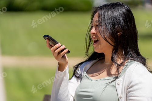 Preview: Happy woman dictating message using voice recognition in the street on a smartphone