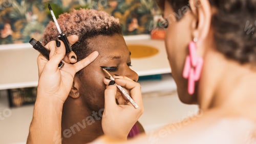 Preview: African transgender man with his eyes closed as a colleague applies make-up