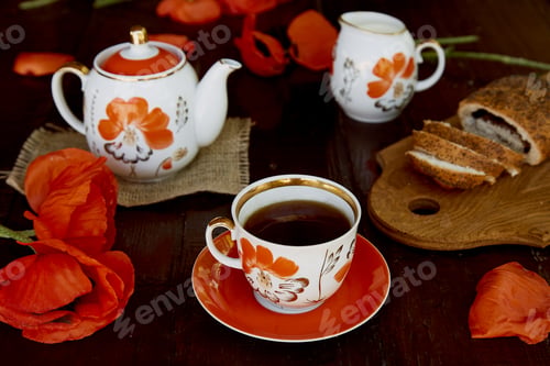 Preview: Traditional poppy seed bun with cup of tea and milk near poppies flowers and dishes