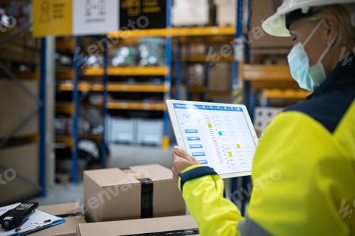 Preview: Young worker with tablet working indoors in warehouse, coronavirus concept.