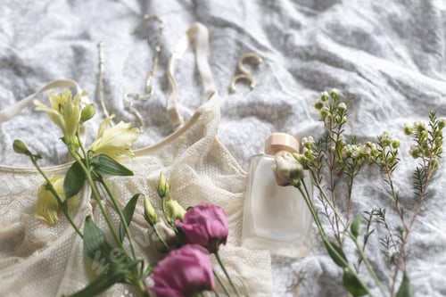 Preview: Stylish lingerie, modern jewelry, perfume bottle and spring flowers on bed. Soft trendy image