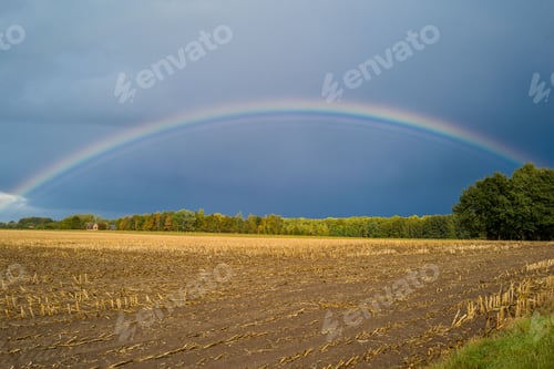 Preview: Breathtaking view of a double rainbow in the sky over a freshly harvested field during a stormy day