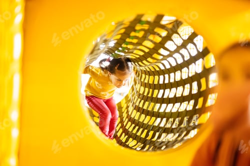 Preview: Little girl move on in pipe at yellow playground park in active entertaiments.