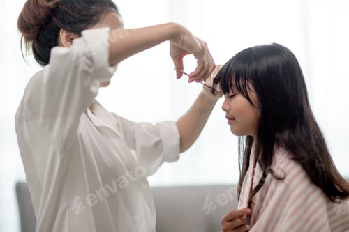 Preview: Asian Mother cutting hair to her daughter in living room at home