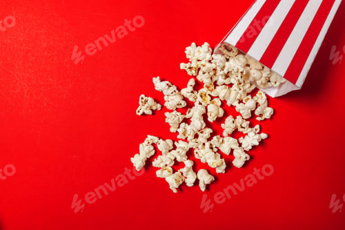 Preview: Popcorn spills from a striped container onto a bright red surface