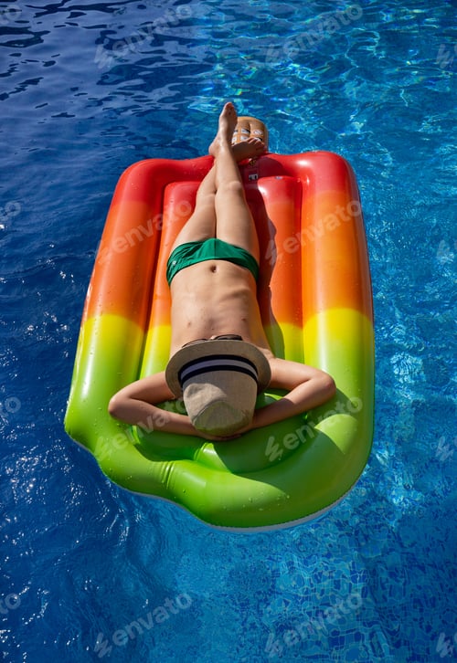 Preview: completely relaxed. boy in a straw hat swims in the pool on an inflatable mattress