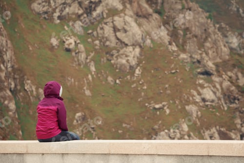 Preview: Solitary girl sitting next to a massive mountain looking to the infinite with copy space