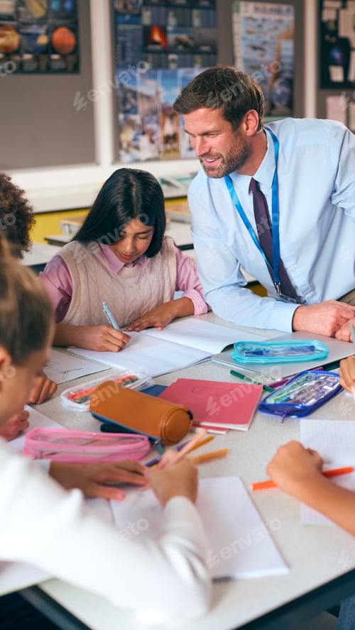 Preview: Male Secondary Or High School Teacher Sitting At Table Working With Students In Classroom
