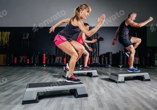 Preview: Woman trainer doing aerobic class with steppers in gym
