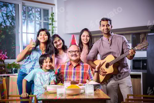 Preview: Indian asian grandparents with Family celebrating birthday by blowing candles on cake at home