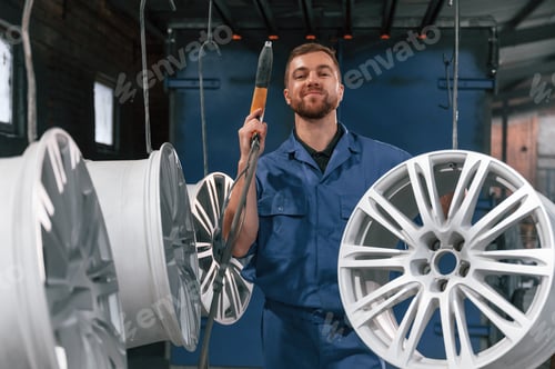 Preview: Holding paint spray gun. Car service station worker is taking care about disks of tires
