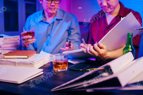 Preview: Two men are working late at office,drinking beer while checking documents.They are overwhelmed