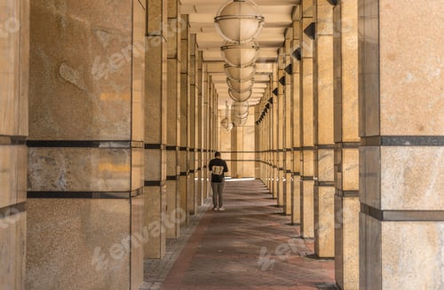 Preview: Wide angle shot of a woman walking between several square columns